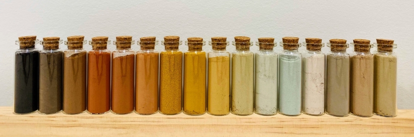 A row of clear bottles filled with colorful soils.